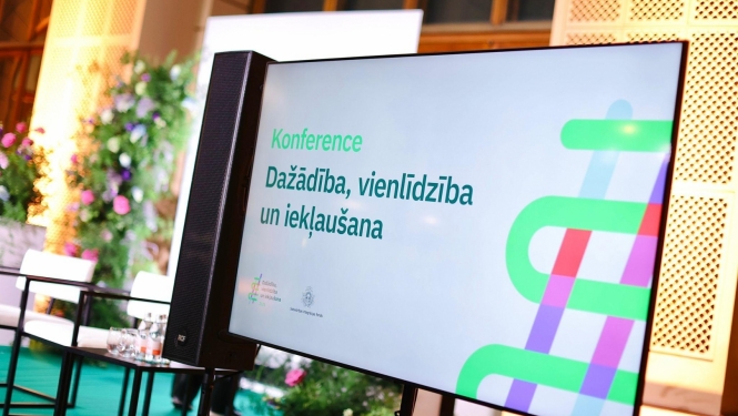 Attēlā ekrāns ar slaidu, kurā ir uzraksts "Konference. Dažādība, vienlīdzība un iekļaušana"