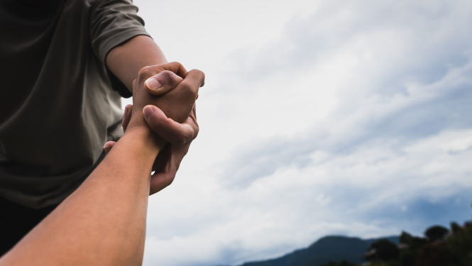 Attēlā redzama rokas pasniegšana un apmākušās debesis