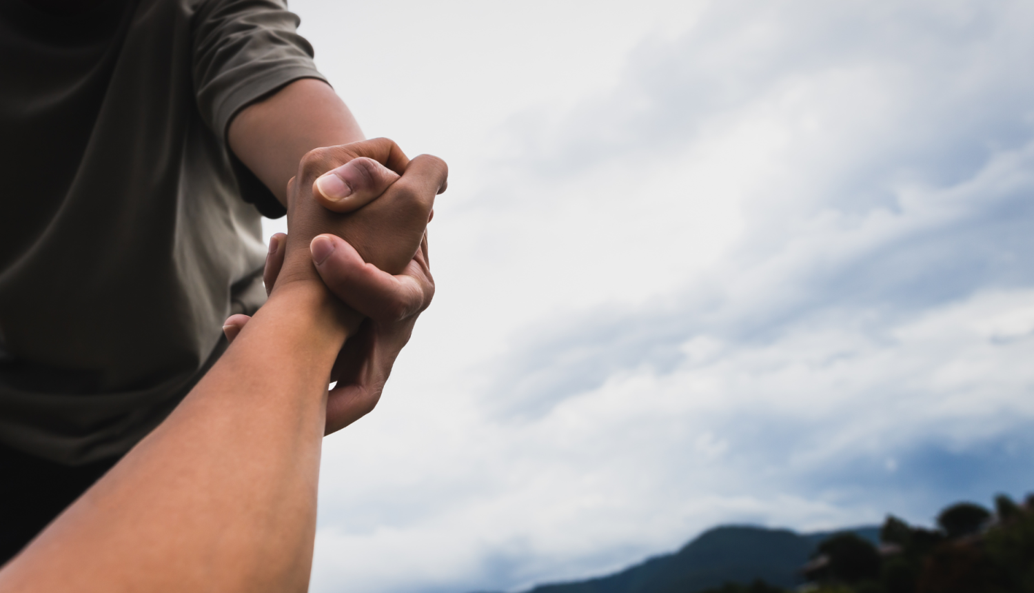 Attēlā redzama rokas pasniegšana un apmākušās debesis