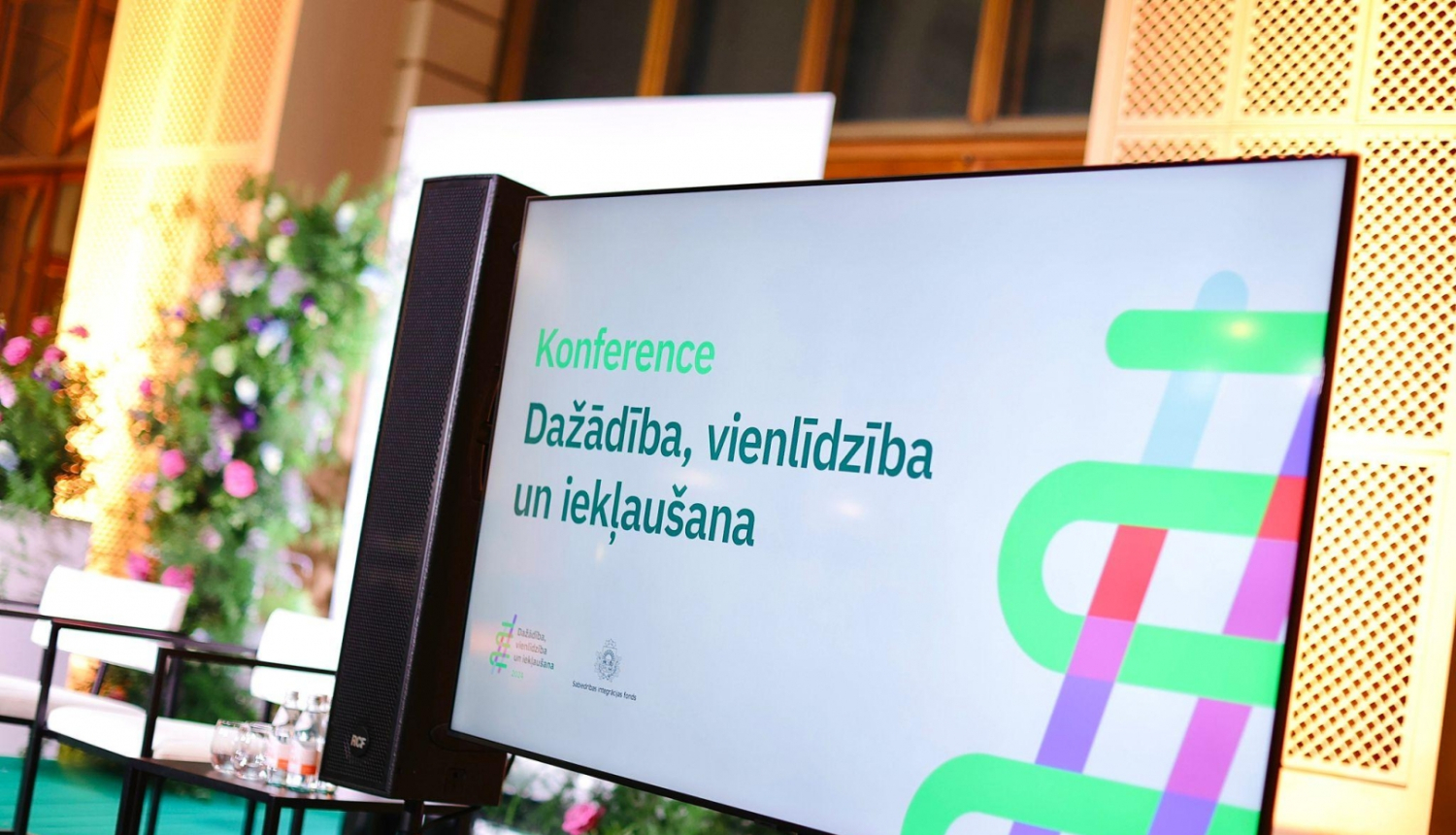 Attēlā ekrāns ar slaidu, kurā ir uzraksts "Konference. Dažādība, vienlīdzība un iekļaušana"