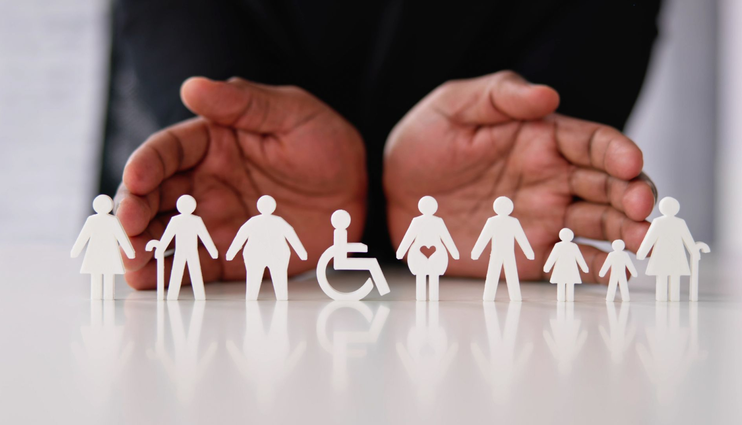 Attēlā redzamas rokas, kuras atbalsta dažādas cilvēku grupas, kuras simbolizē no papīra izgriezti cilvēki