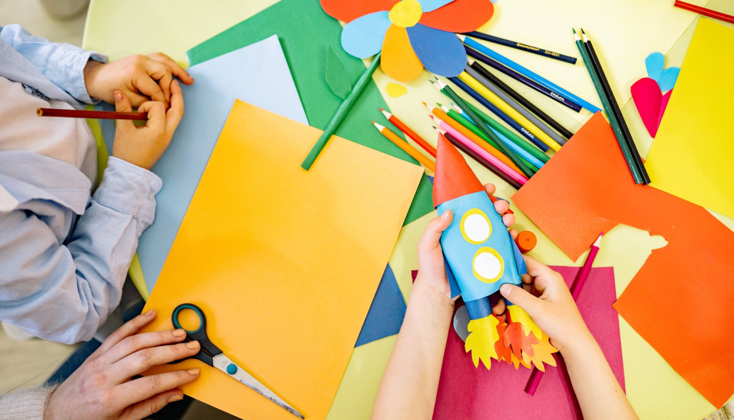 Redzamas skolēnu rokas, kuras no aplikācijas papīra taisa papīra kosmosa kuģi